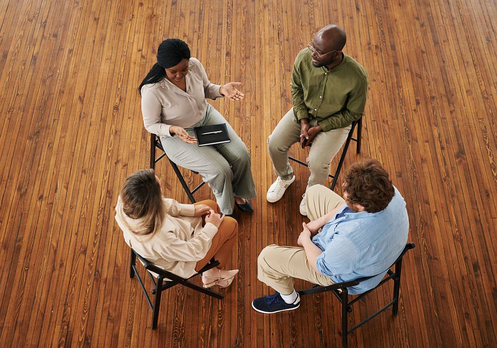 Vier Erwachsene sitzen im Stuhlkreis und sprechen in einer moderierten Gruppensitzung miteinander.