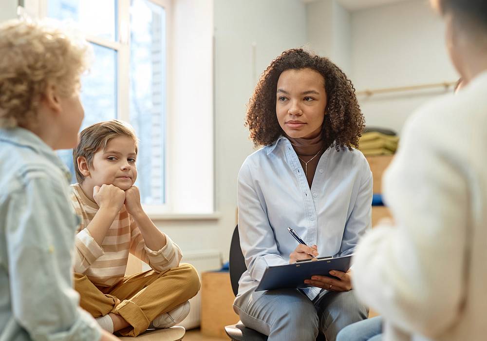 Therapeutin begleitet ein Gespräch mit zwei Kindern und macht aufmerksam Notizen.