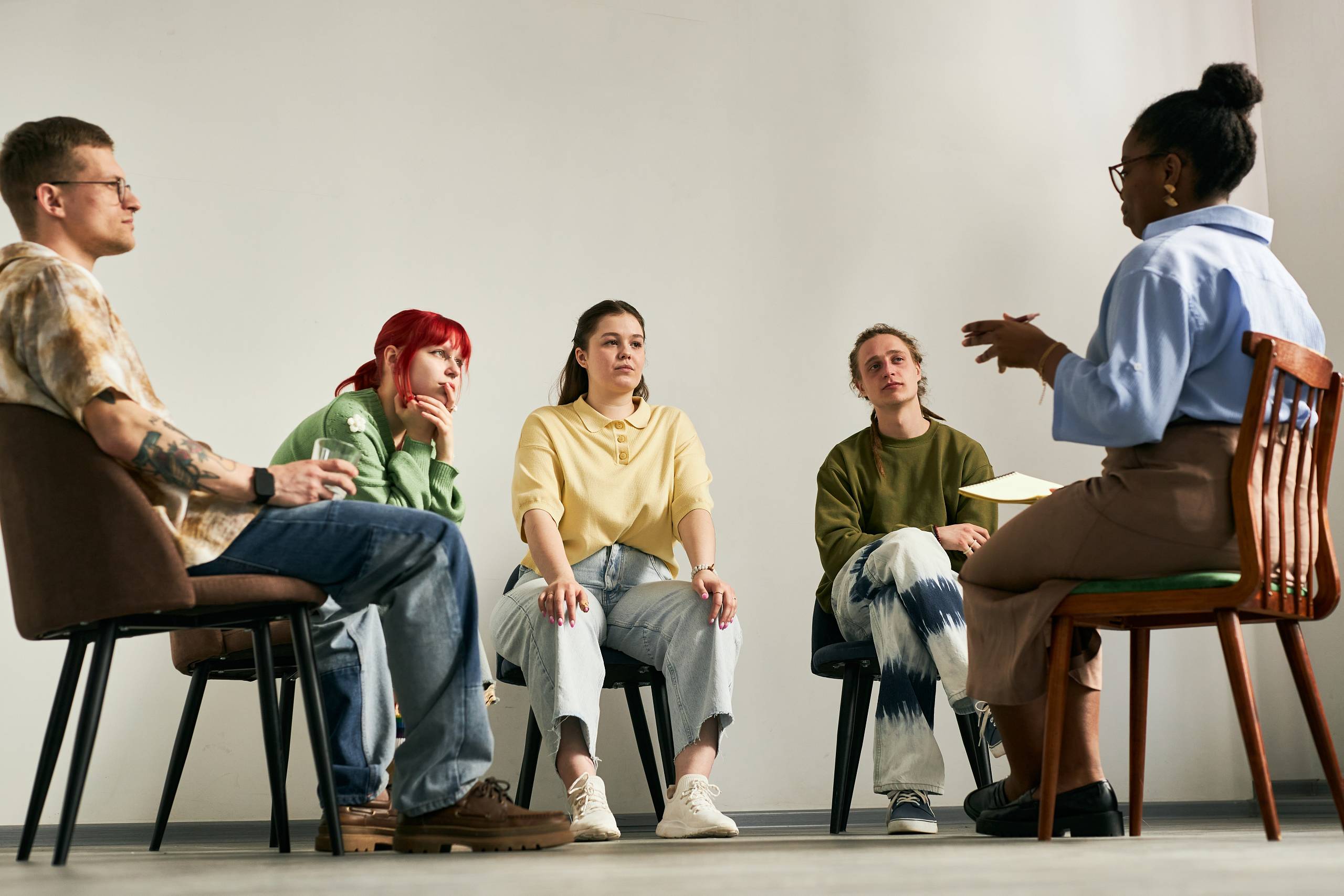 Therapeutin leitet eine Gruppensitzung mit jungen Erwachsenen im Stuhlkreis.