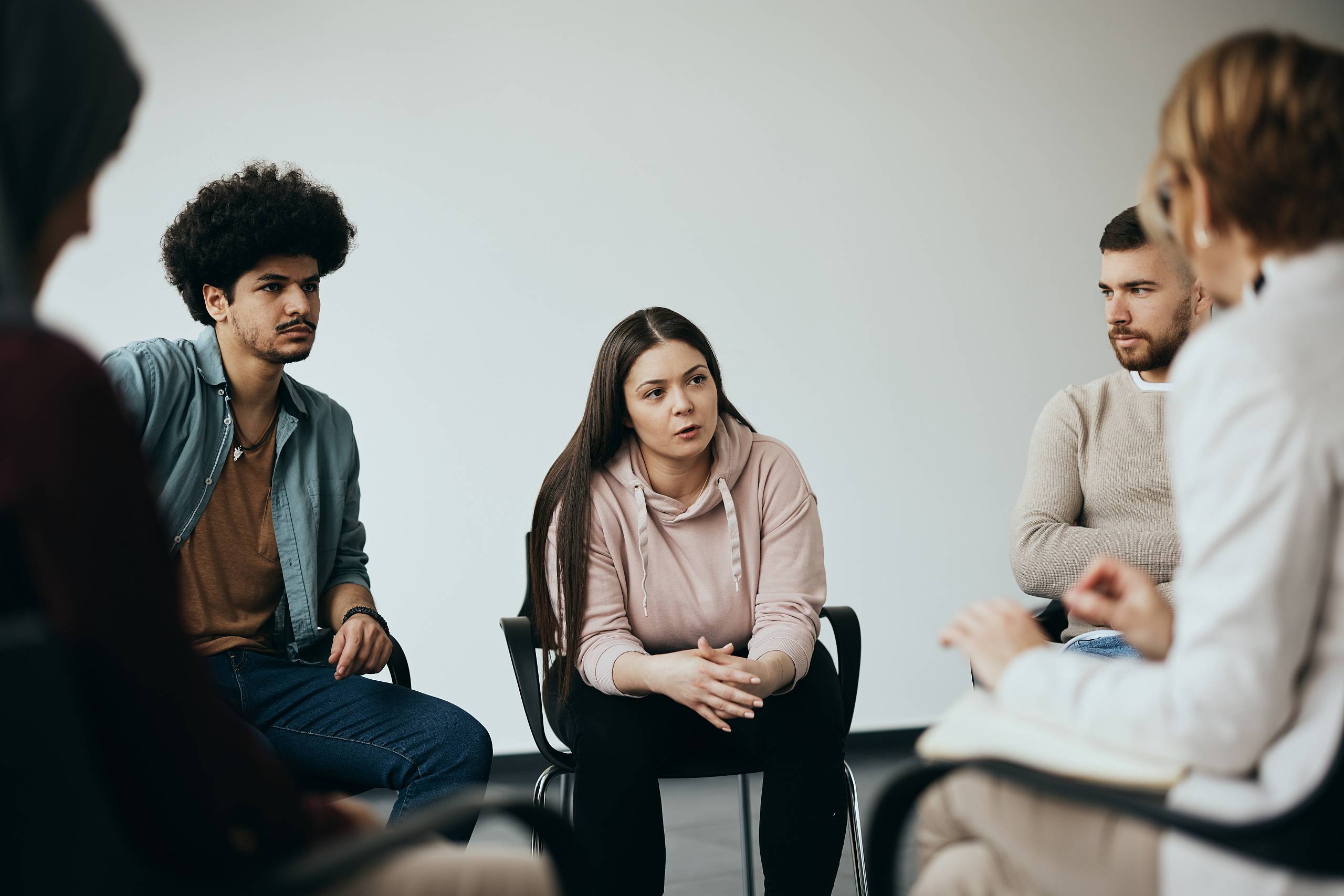 Junge Erwachsene sitzen im Stuhlkreis und hören der Therapeutin in einer Gruppensitzung zu.