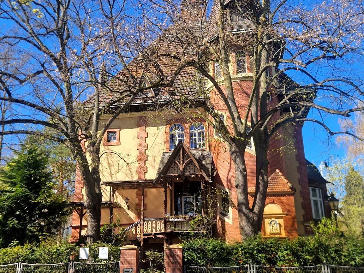 Historisches Institutsgebäude mit Erker, Fachwerkelementen und Garten an einem sonnigen Tag.