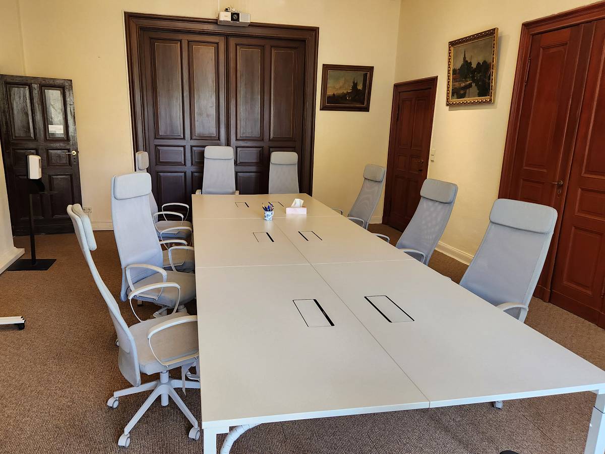 Seminarraum mit großem Konferenztisch, hellen Stühlen und historischen Holztüren.