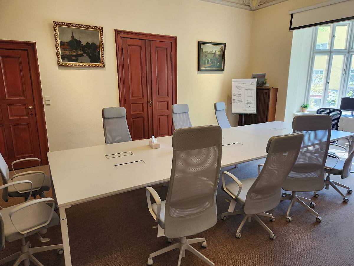 Heller Seminarraum mit Konferenztisch, Flipchart, Leinwand und Blick in den Innenhof.