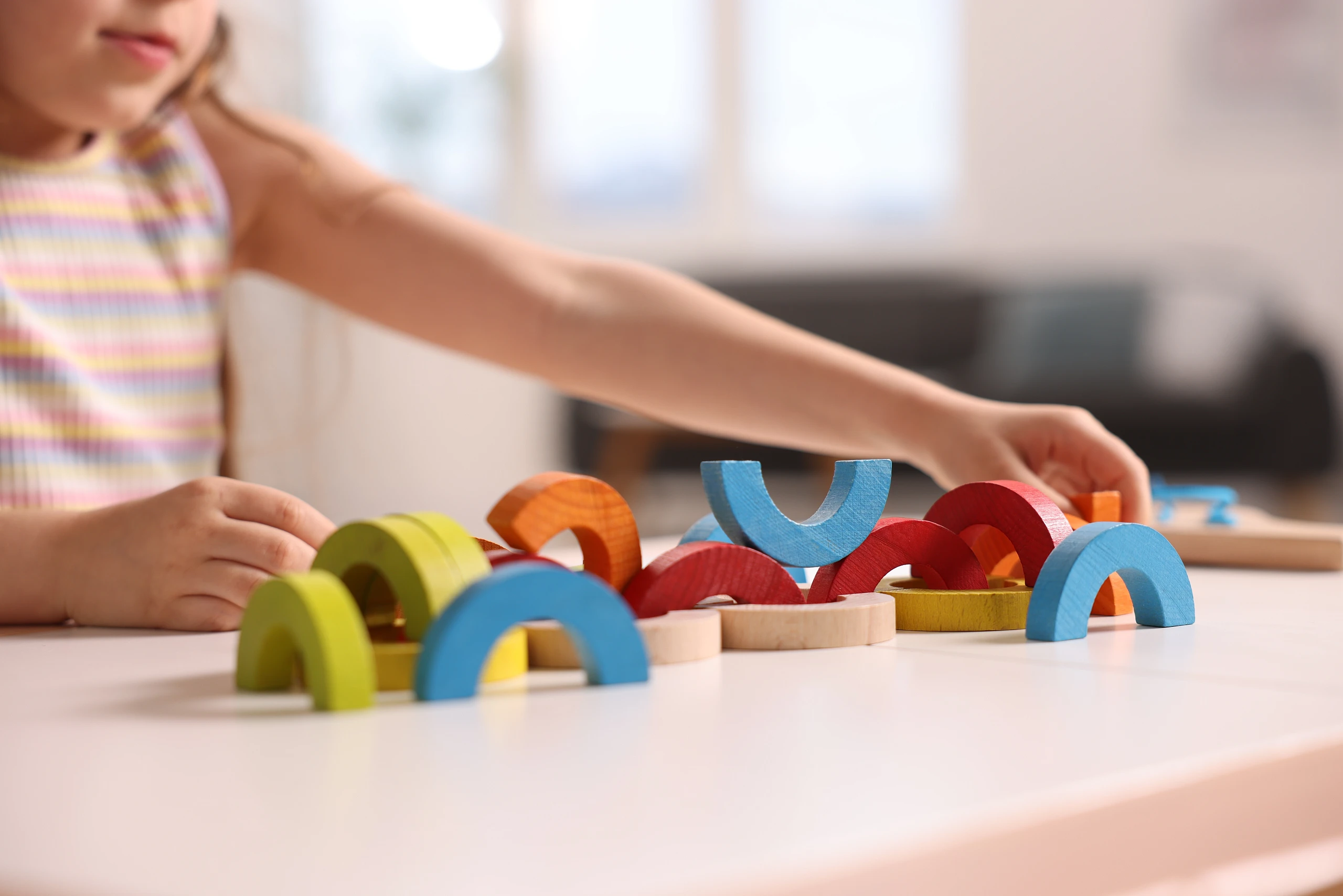 Kind spielt mit bunten Holzbausteinen und trainiert dabei Motorik, Wahrnehmung und Konzentration.