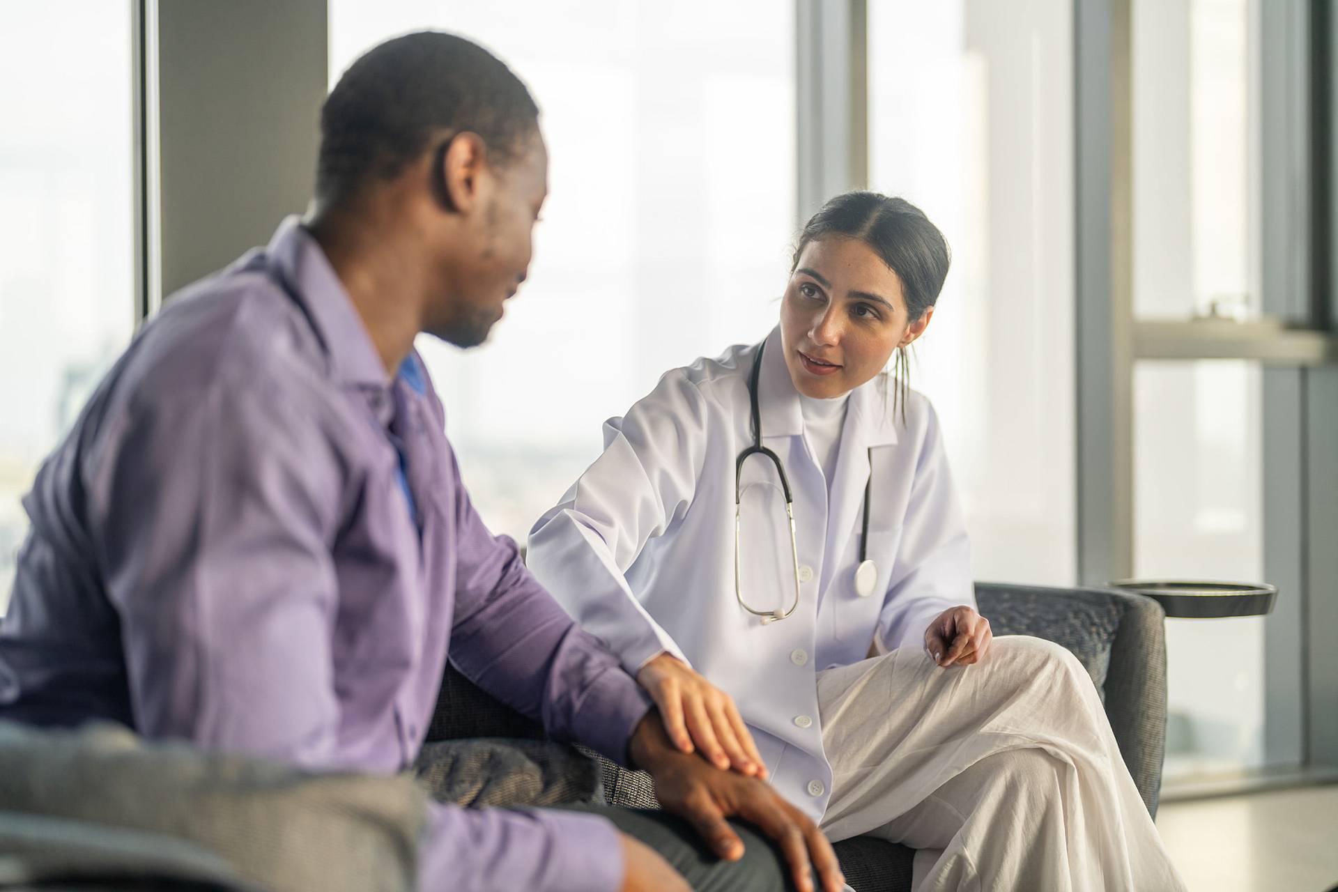 Ärztin spricht einfühlsam mit einem Patienten in einem hellen Beratungsbereich.