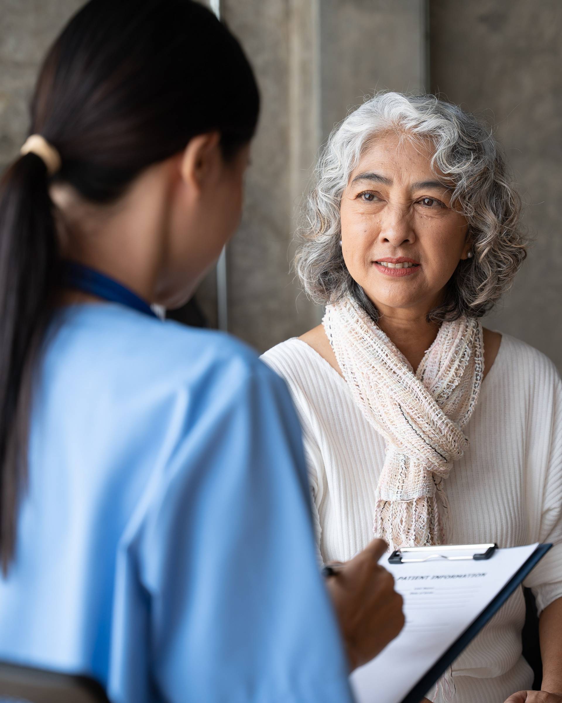 Ärztin macht Notizen im Gespräch mit einer älteren Patientin in einem ruhigen Beratungsraum.