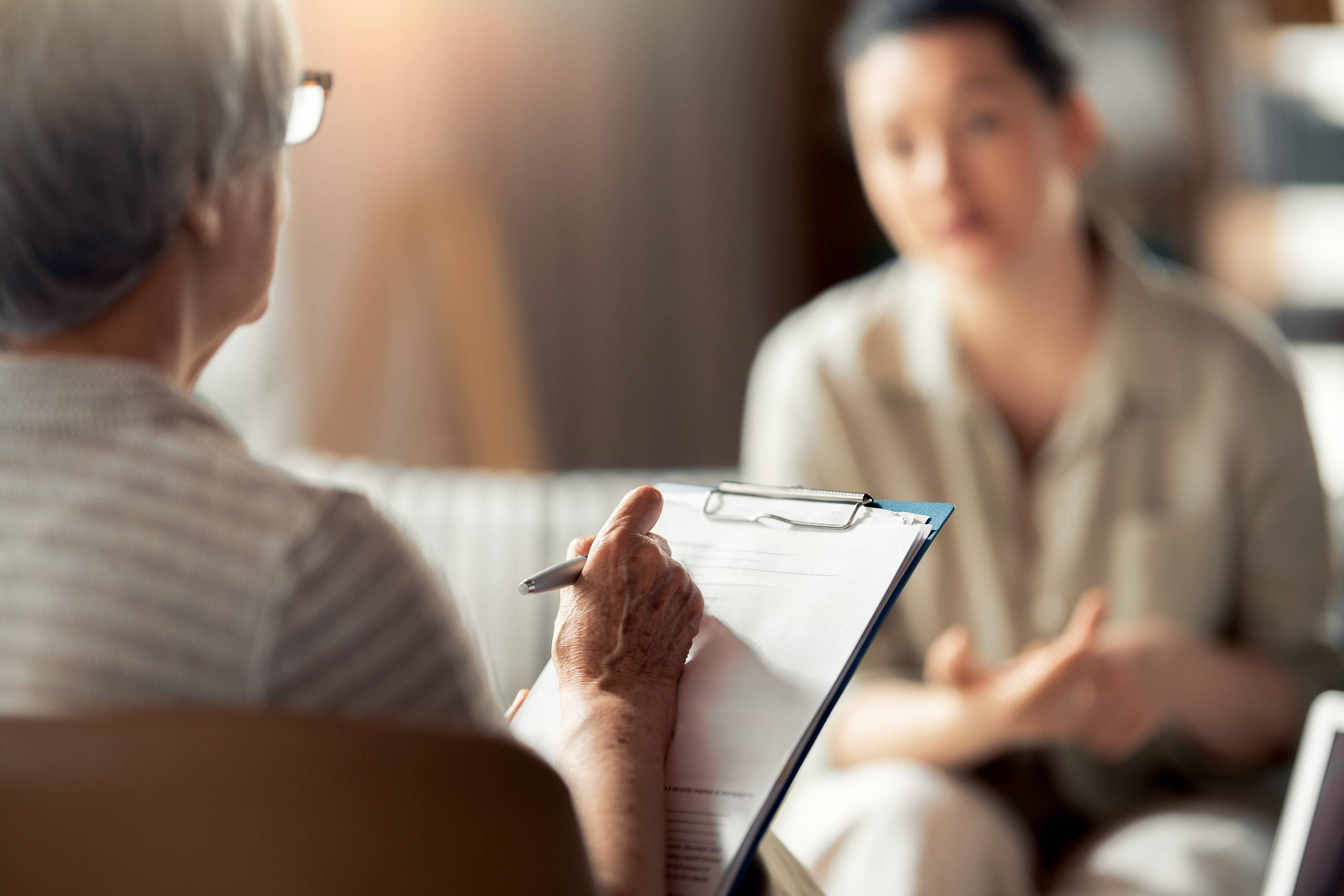 Ärztin hält Klemmbrett im Beratungsgespräch, während eine Patientin ihre Situation schildert.